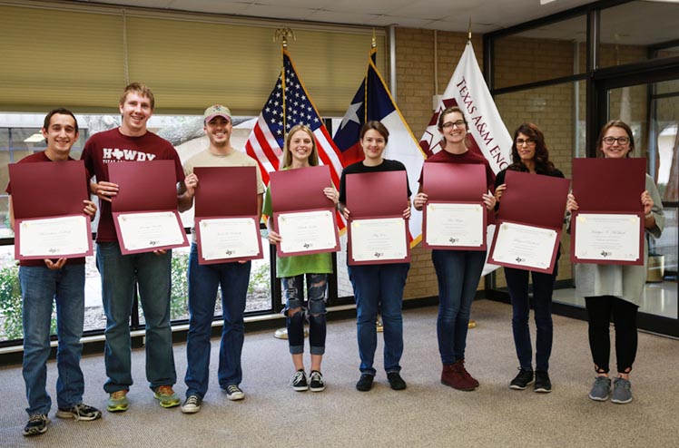 Students standing with certificates in front of the US, Texas, and TEEX flags.