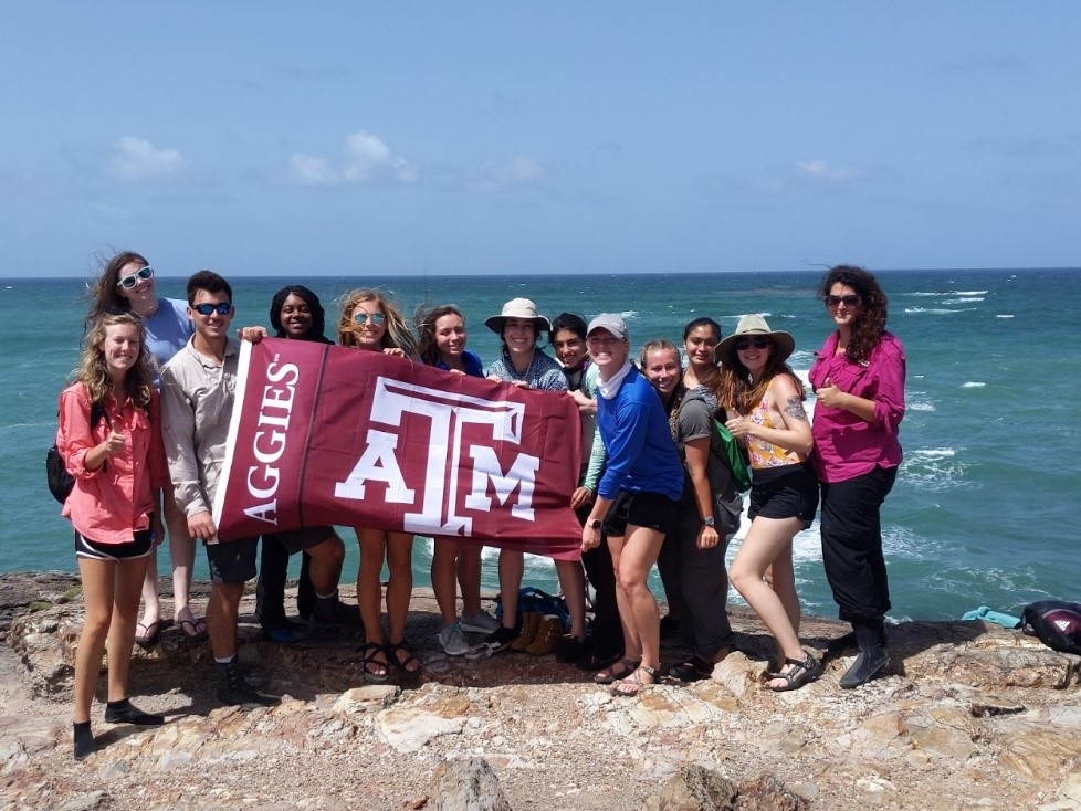 Students holding the Aggie flag on the beach